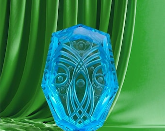 May include: A faceted, light blue crystal with intricate etched patterns. The crystal is a vibrant shade of blue and has a symmetrical design with circles and lines. The background is a solid green color.