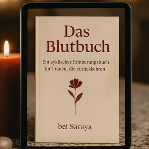 May include: A book titled "Das Blutbuch" is displayed in a black frame. The cover is beige with burgundy text and a floral illustration. The text reads "Ein zyklisches Erinnerungsbuch für Frauen, die zurückkehren" and "bei Saraya".