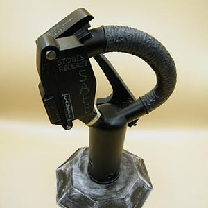 May include: A black metal device with a handle and a base. The device has the words "STORES RELEASE SAFE" printed on it. The base is an octagon shape with a distressed, white-painted finish.