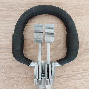 May include: A black, padded, semi-circular handle with two silver-colored, rectangular pedals. The pedals have a textured surface. The base of the device is silver-colored and has a cylindrical shape.