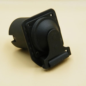 Op de afbeelding: Een zwarte aanhangerconnector met een vierkante montageplaat en een cilindrische socket. De connector heeft een scharnierende klep en is ontworpen voor elektrische aansluitingen. Het item is gemaakt van duurzaam plastic.
