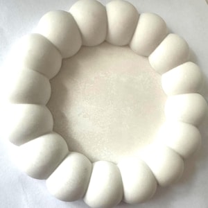 Può includere: Un vassoio circolare bianco caratterizzato da un bordo rialzato, arrotondato e simile a bolle che circonda un centro liscio e piatto. L'intero oggetto presenta una finitura bianca opaca e uniforme, creando un'estetica pulita e morbida.