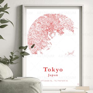 May include: A framed print featuring a red line map of Tokyo, Japan. The city map is set against a white background. The word "Tokyo" and "Japan" are printed in red below the map. The print is displayed near a green sofa and plant.