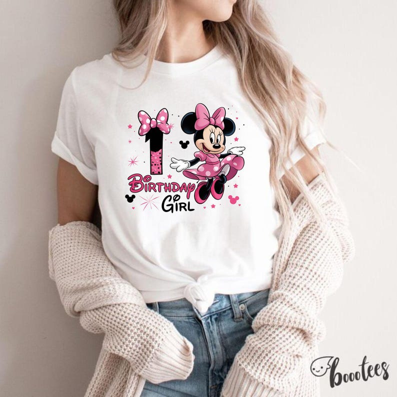 May include: White t-shirt with a Minnie Mouse graphic. The design includes a number 1, a pink bow, and the words "Birthday Girl." Minnie Mouse is in a pink polka-dot dress. The shirt is a casual style, suitable for a birthday celebration.