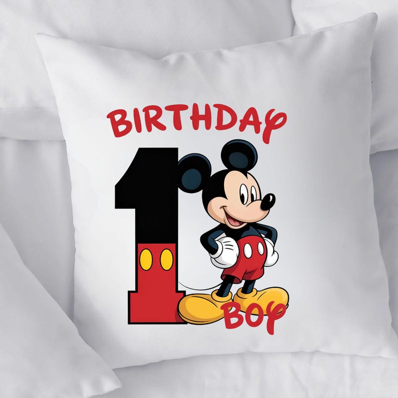 May include: White square pillow featuring a colorful graphic of Mickey Mouse. The design includes the number "1", the words "BIRTHDAY BOY", and Mickey Mouse in his classic outfit. The pillow is likely for a child's first birthday.