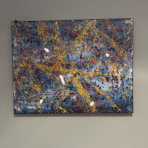 Puede incluir: Pintura expresionista abstracta sobre lienzo. La obra presenta un fondo azul oscuro con salpicaduras de pintura amarilla, roja y blanca. La pintura es rectangular y está montada sobre un marco de madera.
