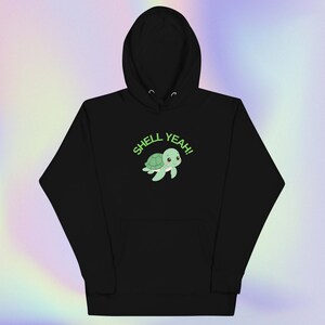 May include: Black hooded sweatshirt with a front graphic. The graphic features a cartoon turtle with the text "SHELL YEAH!" in green. The turtle is light green with a white belly. The sweatshirt has a front pocket and a hood with drawstrings.