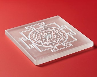 Puede incluir: Un posavasos cuadrado y translúcido con un diseño geométrico blanco. El posavasos está hecho de un material transparente y se encuentra sobre una superficie roja. El diseño es un patrón simétrico detallado.