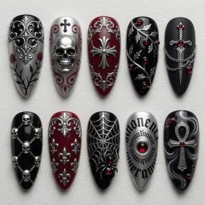 May include: A set of ten long, almond-shaped artificial nails with gothic-inspired designs. The nails feature silver embellishments, skulls, crosses, spiderwebs, and ornate patterns on a variety of colors, including black, red, and silver.