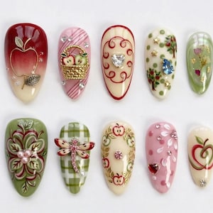 以下が含まれることがあります： 様々なデザインの人工爪10個のコレクション。爪には、リンゴ、花の模様、装飾的な装飾など、詳細なアートワークが施されています。色は赤、ピンク、緑、金で、光沢のある仕上がりです。デザインは複雑で芸術的です。