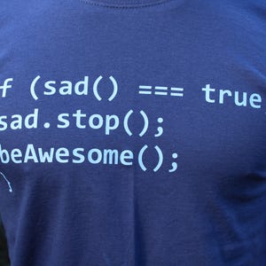 Peut inclure: T-shirt bleu marine avec texte bleu clair. Le texte dit : "if (sad() == true) sad.stop(); beAwesome();". Un design amusant pour les codeurs et les passionnés d'informatique.