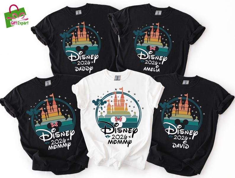 May include: Five black and white t-shirts with a Disney castle design. The shirts have the text "Disney 2026" and names "Daddy", "Amelia", "Mommy", and "David". The design includes a castle, Mickey Mouse ears, and a colorful sunset.