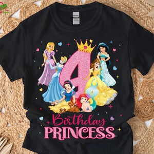 Pu&ograve; includere: T-shirt nero con grafica di principesse Disney, un grande numero 4 rosa e la scritta "Birthday PRINCESS". Le principesse indossano abiti colorati, con una corona d'oro sopra il numero.