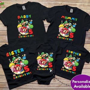 May include: Black family birthday t-shirts featuring a colourful graphic of video game characters. The shirts read "Daddy", "Mummy", "Sister", "Brother", and "Birthday Boy" with the number "5". A baby onesie is also included.