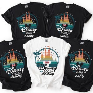 May include: Five black and white t-shirts with a Disney castle design. The shirts have the text "Disney 2026" and names "Daddy", "Amelia", "Mommy", and "David". The design includes a castle, Mickey Mouse ears, and a bow.
