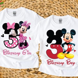 Puede incluir: Dos camisetas blancas con diseños de Mickey y Minnie Mouse. Una camiseta presenta a Minnie Mouse con un lazo y un vestido de lunares rosas, el número 3 y el texto "Birthday Girl". La otra camiseta tiene a Mickey Mouse, el número 3 y el texto "Birthday Boy".