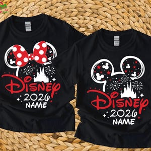 May include: Two black t-shirts with a Disney design. One features a red polka dot bow, the other has red stars. Both shirts have a white Mickey Mouse head outline, the word "Disney" in red, "2026", and space for a name.