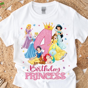 Pu&ograve; includere: T-shirt bianca con un numero 4 rosa glitterato, una corona d'oro e principesse dei cartoni animati. Il testo "Birthday Princess" &egrave; in lettere rosa glitterate sotto le principesse.