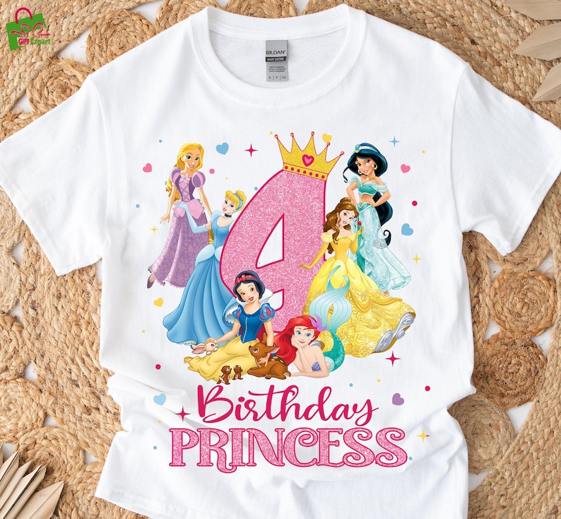 Pu&ograve; includere: T-shirt bianca con un numero 4 rosa glitterato, una corona d'oro e principesse dei cartoni animati. Il testo "Birthday Princess" &egrave; in lettere rosa glitterate sotto le principesse.