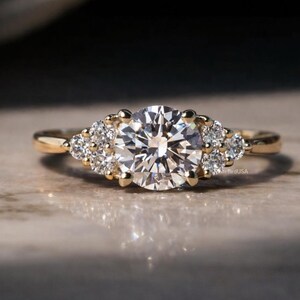 May include: A gold ring featuring a large, round, clear gemstone as the focal point, flanked by smaller, clear gemstones. The ring has a classic design with a polished gold band. The setting highlights the brilliance of the gemstones.