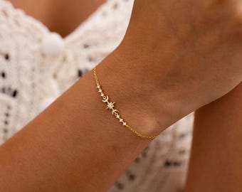 May include: A delicate gold chain bracelet featuring a central charm arrangement of a small crescent moon, a starburst, and several tiny round clear stones. The bracelet is constructed with a fine link chain and a secure clasp mechanism.