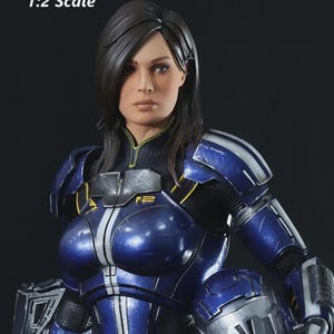 May include: A detailed 1:2 scale figure of a woman in a futuristic blue and silver armored suit. The figure has dark hair and a serious expression. The armor features white stripes and yellow accents.
