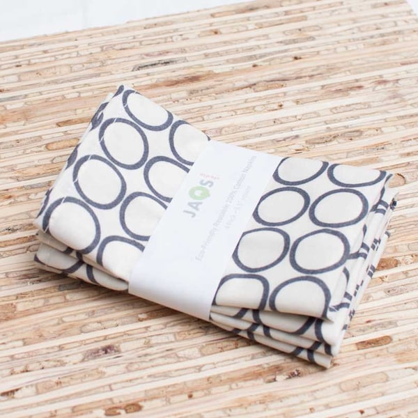 May include: A stack of three white fabric napkins with a black and white geometric pattern of circles. The napkins are packaged with a white label that reads "JAOS - 100% Premium Organic Cotton Napkins - Made in USA".