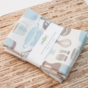 Puede incluir: Un conjunto de cuatro toallas de cocina de algod&oacute;n azul y blanco con un patr&oacute;n marr&oacute;n y blanco de utensilios de cocina y una etiqueta que dice "JAOS Eco-Friendly Reusable Cotton Napkins 4 Pack - 16.5" square"