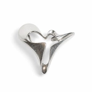 May include: A polished silver-tone brooch featuring an abstract, fluid, and open-work design with smooth, curved edges and a pointed, elongated tail. The metallic surface reflects light, highlighting the continuous, flowing form of the piece.
