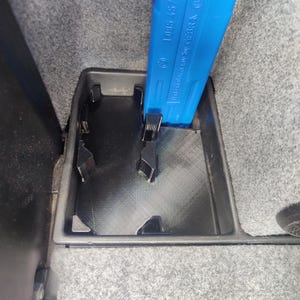 May include: A black plastic storage compartment with a blue tool inserted. The tool is labelled "1095 457" and "Made in Germany by GEBRA". The compartment is set in a grey, textured surface.