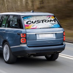 Könnte beinhalten: Ein blauer SUV mit einer individuellen Heckscheibengrafik. Die Grafik zeigt das Wort "CUSTOM" in Weiß, vor einem farbenfrohen Farbspritzer und einem gepunkteten Hintergrund. Das Fahrzeug ist in Bewegung.