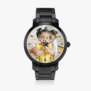 Puede incluir: Reloj de pulsera negro con esfera redonda que muestra una fotograf&iacute;a de dos ni&ntilde;os peque&ntilde;os. El reloj tiene una correa y un bisel de metal negro. Las manecillas del reloj indican la hora. Un accesorio de moda.