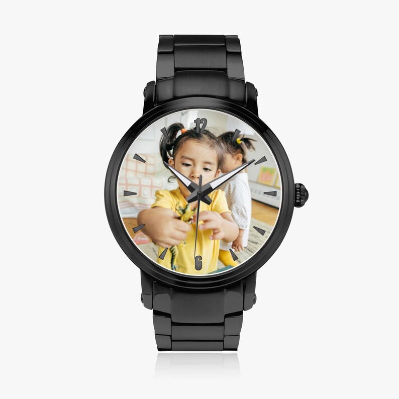 Puede incluir: Reloj de pulsera negro con esfera redonda que muestra una fotograf&iacute;a de dos ni&ntilde;os peque&ntilde;os. El reloj tiene una correa y un bisel de metal negro. Las manecillas del reloj indican la hora. Un accesorio de moda.