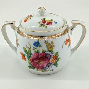 May include: White porcelain sugar bowl with lid, featuring a gold rim and handles. The bowl is decorated with colorful floral patterns, including pink, red, orange, and blue flowers. The lid has a small gold finial.