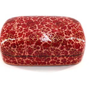 May include: A rectangular lidded box with rounded corners, featuring a glossy finish and a dense, repeating pattern of dark red flowers with thin gold outlines set against a lighter pink background, creating a vibrant and detailed surface.