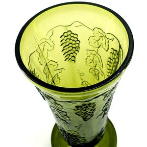 Op de afbeelding: Groene glazen vaas met druiven- en bladerenontwerp. De vaas heeft een brede opening en een ronde basis. Het druiven- en bladerenpatroon is in het glas ge&euml;tst. De vaas heeft een lichtgroene kleur.