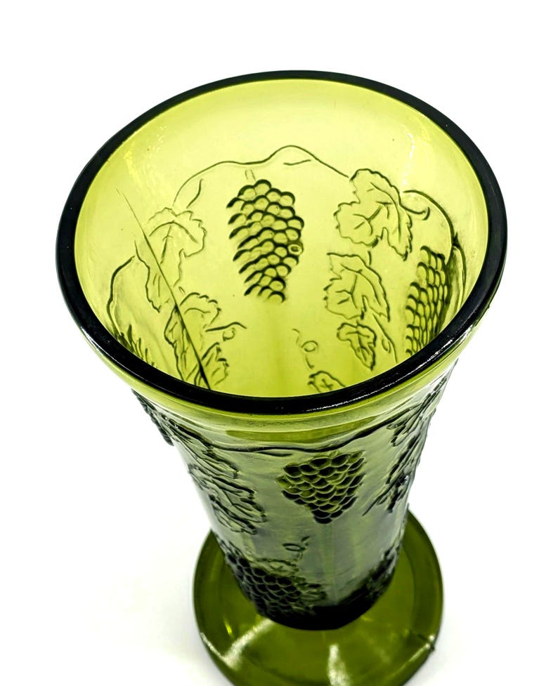 Op de afbeelding: Groene glazen vaas met druiven- en bladerenontwerp. De vaas heeft een brede opening en een ronde basis. Het druiven- en bladerenpatroon is in het glas ge&euml;tst. De vaas heeft een lichtgroene kleur.