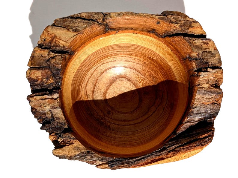 K&ouml;nnte beinhalten: Handgefertigte Holzschale mit nat&uuml;rlicher Kante. Das Innere der Schale ist warmbraun mit sichtbarer Holzmaserung, w&auml;hrend die Au&szlig;enseite eine raue, strukturierte Rinde aufweist. Ein einzigartiges Dekorationsst&uuml;ck.