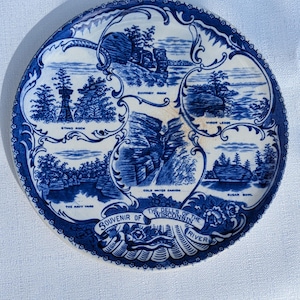 May include: A round, blue and white souvenir plate featuring scenic illustrations of the Wisconsin River Dells. The plate includes text such as "Chimney Rock", "Stand Rock", and "Sugar Bowl". The border has a decorative pattern.