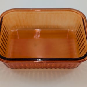 May include: Amber-colored rectangular baking dish with ribbed sides and a smooth interior. The dish has a dark rim and is made of glass. A classic kitchenware item.