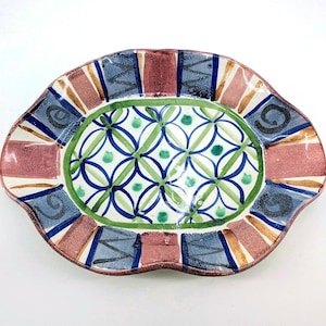 May include: Oval ceramic serving platter with a scalloped edge. The platter features a colorful design with a central pattern of green and blue interlocking circles. The border has alternating sections of blue, red, and cream colors.