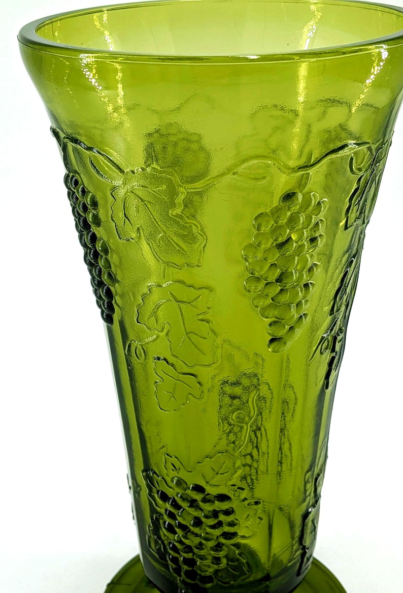 Op de afbeelding: Groene glazen vaas met een reli&euml;f van druiven en bladeren. De vaas heeft een uitlopende bovenkant en een ronde basis. Het druivenpatroon herhaalt zich rond de vaas. Het glas heeft een getextureerd oppervlak.