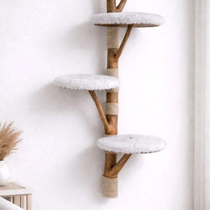 May include: A wall-mounted cat tree with three circular platforms covered in white, fluffy material. The platforms are supported by wooden branches attached to a central wooden pole wrapped with natural rope. The cat tree is designed to be mounted on a white wall.
