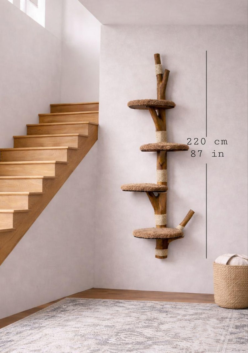 May include: A wooden cat tree with four circular platforms and a natural, rustic design. The cat tree is 87 inches (220 cm) tall and is mounted on a white wall. The platforms are covered in a soft, brown material.