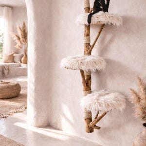 May include: A cat tree with three levels, made of natural wood and faux fur. A black and white cat sits on the top level. The cat tree is mounted on a white wall, with a neutral-toned interior in the background.