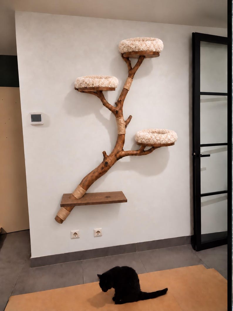 May include: A wall-mounted cat tree constructed from a natural wooden branch with a dark brown finish. It features three circular platforms topped with plush, cream-colored cushions and one rectangular wooden shelf. Sections of the branch are wrapped in light tan rope.
