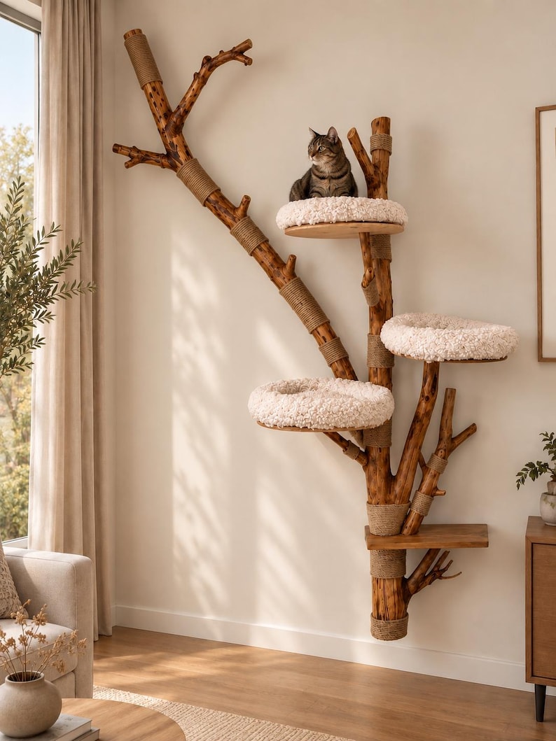 May include: A wall-mounted cat tree constructed from a natural wooden branch with multiple levels. It features three circular platforms topped with plush, cream-colored fabric cushions and one flat wooden shelf. Sections of the branch are wrapped in tan rope.