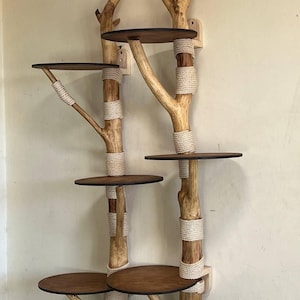 May include: A wall-mounted cat tree with a natural, rustic design. It features wooden branches with circular platforms and is wrapped with rope. The platforms are made of dark brown wood. The cat tree is designed to be mounted on a wall.