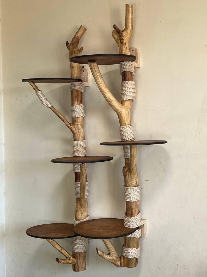 May include: A wall-mounted cat tree with a natural, rustic design. It features wooden branches with circular platforms and is wrapped with rope. The platforms are made of dark brown wood. The cat tree is designed to be mounted on a wall.