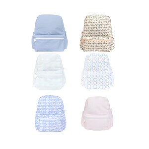 May include: A collection of six backpacks in various colors and patterns. The backpacks include solid light blue, white, and pink, as well as patterned designs in beige, blue, and white. Each backpack has a front pocket and a zipper closure.